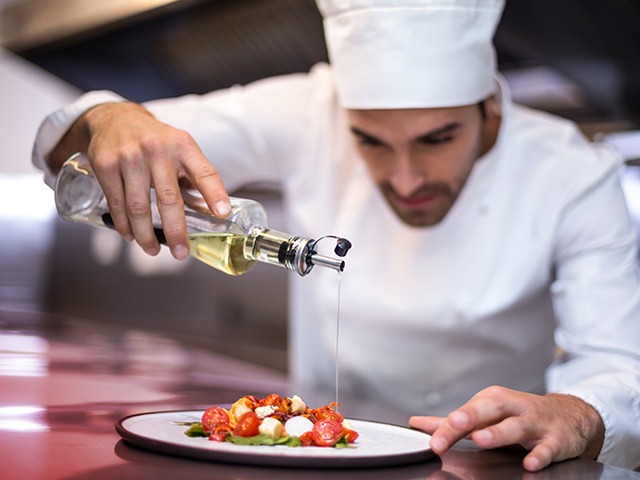 A chef pouring olive oil over a salad