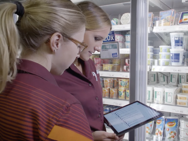 Two women looking at a tablet in front of a supermarket cooler